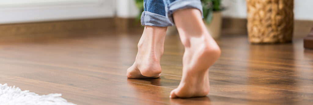 Frau geht mit nackten Füßen über den Fußboden ihrer Wohnung